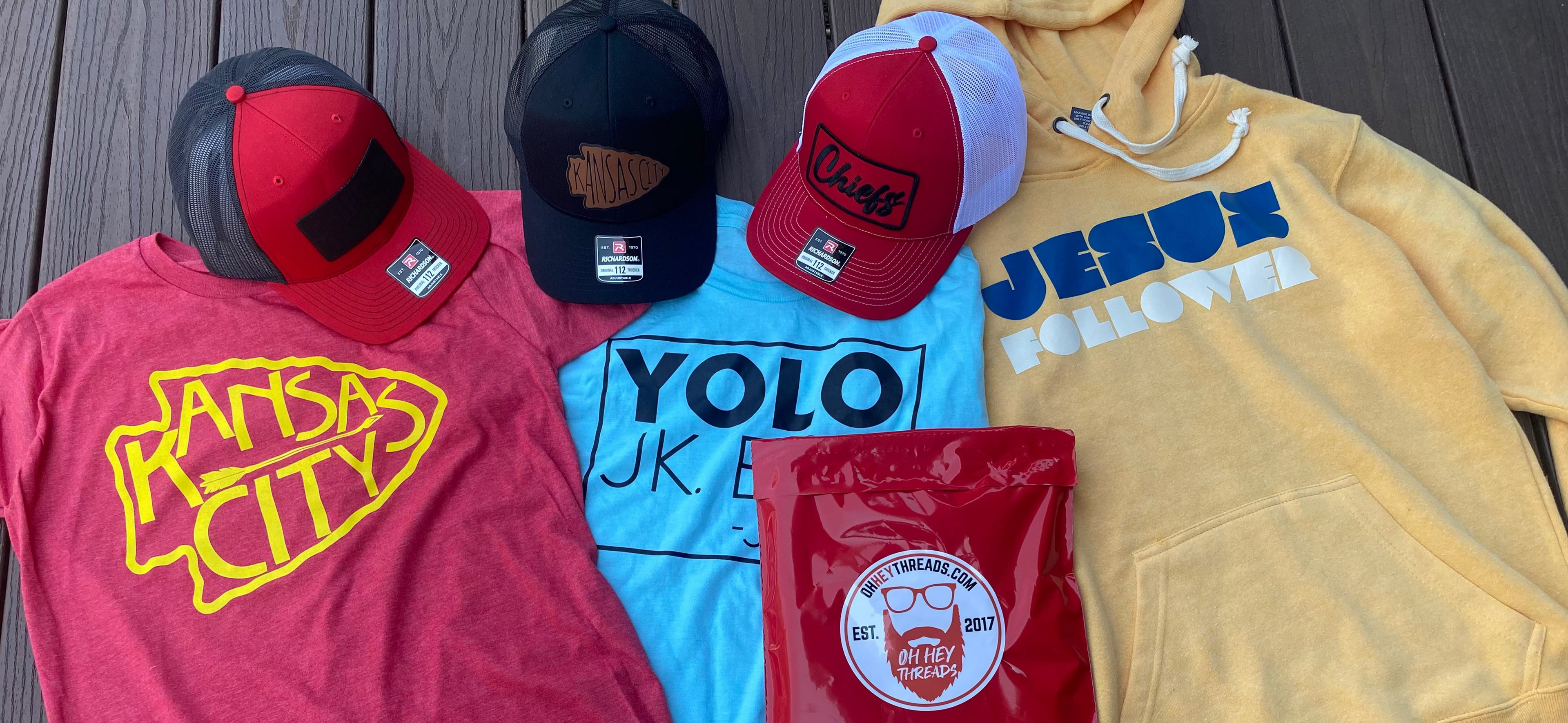 Collection of clothing items including t-shirts, caps, and a hoodie on a wooden surface.